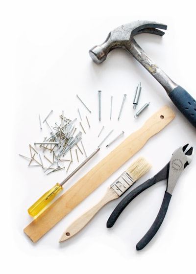 Hammer, screwdriver, pliers, nails and a folding rule laid out on a white surface