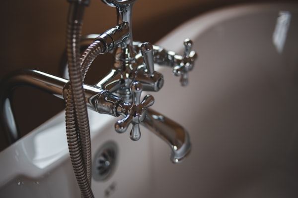 Close-up of chrome bath taps and a shower hose over a white bath